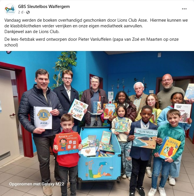 Foto met enkele Lions leden, de schooldirecteur, en enkele kinderen. Iedereen staat rond de bakfiets met nieuwe leesboeken